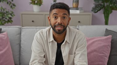 Hoş bir oturma odasında gülümseyen sakallı yakışıklı bir adam, rahat, modern bir ev hayatı tasvir ediyor..