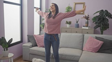 Neşeli genç bir kadın, rahat bir oturma odasında kolları açık, yerde kabarık beyaz bir köpekle uzanıyor..