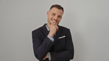 Takım elbiseli yakışıklı genç adam beyaz bir arka plana güvenerek gülümsüyor.