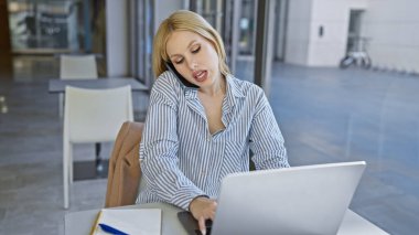 Çizgili tişörtlü genç sarışın bir kadın şehir merkezinde bir kafede dizüstü bilgisayar kullanıyor..