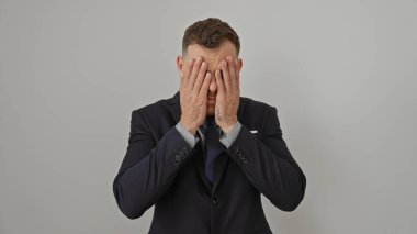 Stresli bir iş adamı, beyaz bir arka plana karşı takım elbise giyip ellerini yüzünü kapatır..