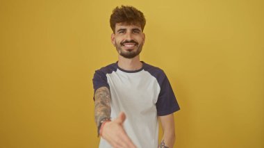 Yakışıklı sakallı adam, parlak sarı arka planda el sıkışmak için elini uzatıyor.