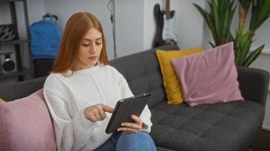 Genç bir kadın rahat bir oturma odasında tabletini karıştırıyor, rahat ve modern bir ev ortamı yayıyor..