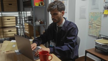 Polis karakolunda dizüstü bilgisayarda çalışan yakışıklı İspanyol bir adam. Kupa, rozet ve haritayla ayarlanmış.