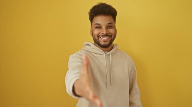 Sarı arka planda elini uzatan, sıcaklığı ve dostluğu tasvir eden, gündelik kıyafetli yakışıklı bir adam..