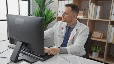 Steteskoplu beyaz önlüklü İspanyol adam klinikte bilgisayar kullanıyor.