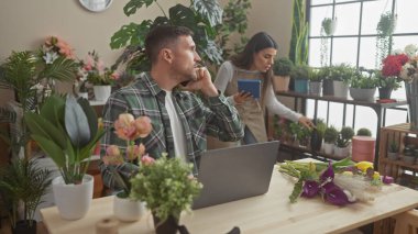 Bir erkek ve bir kadın canlı bitkilerin arasında birlikte çalışıyorlar. Parlak, yeşil, kapalı bir çiçekçide..
