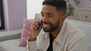 Yakışıklı sakallı adam rahat, modern bir oturma odasında akıllı telefondan konuşuyor.