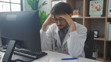 Klinikteki beyaz önlüklü sakallı, stresli genç adam.