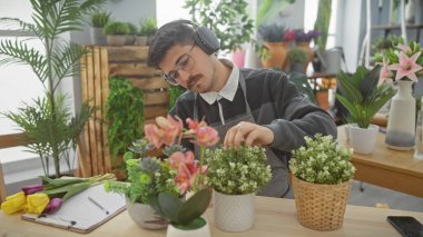 Odaklanmış, bıyıklı genç bir İspanyol, bitkilerle dolu bir çiçekçide çiçek düzenliyor..