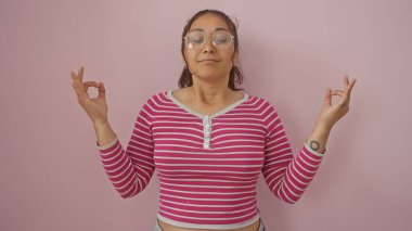 A serene young hispanic woman meditates against a pink wall, her beautiful composure embodying relaxation and mindfulness. clipart