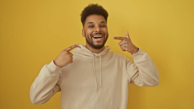 Neşeli bir siyah adam, gülüşünü sarı bir arka planda gösteriyor, pozitiflik ve kendine güveni resmediyor..