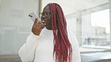 Örgü ören Afro-Amerikalı kadın şehir ortamında akıllı telefon kullanıyor.