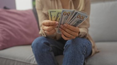 Genç bir kadın oturma odasındaki bir kanepede oturmuş ev dekorunu gösterirken bize dolar sayıyor..