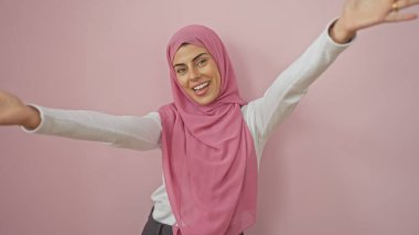 Kolları açık, pembe arka planda tesettürlü mutlu Müslüman kadın.