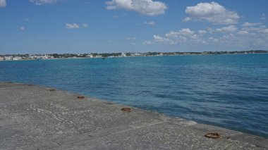 Puglia, İtalya 'daki Porto Sezaryo rıhtımından sakin deniz manzarası güneşli bir günde berrak mavi sular ve uzak bir kıyı şeridi..