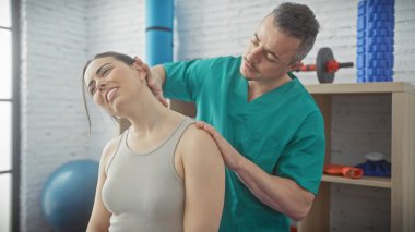 Erkek bir fizyoterapist, bir rehabilitasyon kliniğinde bir kadının omzunu tedavi eder. Bakım, sağlık ve sağlığını yansıtır..