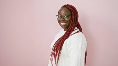 Saçları örgülü, pembe izole bir arka planda gülümseyen, gözlüklü Afrikalı Amerikalı bir kadın..