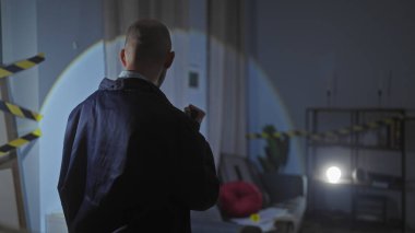 İçerideki karanlık bir suç mahallinde kel bir adam. Dikkat bandı, spot ışığı ve mobilyalarla..