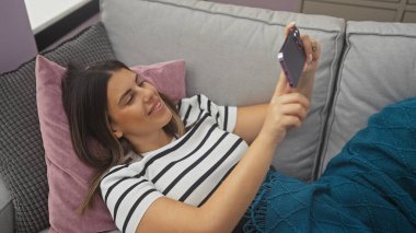 Genç bir kadın, modern bir evde akıllı telefonuyla selfie çekiyor..