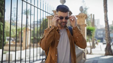 Yakışıklı İspanyol genç adam güneşli bir şehir ortamında güneş gözlüğünü ayarlıyor.