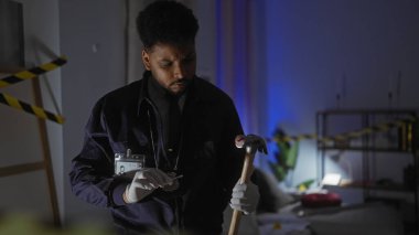 Afro-Amerikalı bir adam çekiçle bir suç mahallini inceliyor. Kapalı mekandaki loş bir mekanda kanıt olarak..