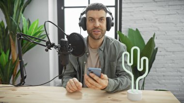 Stüdyoda sakallı yakışıklı, akıllı telefon tutan, mikrofon ve kaktüs ışığıyla kulaklık takan bir İspanyol..