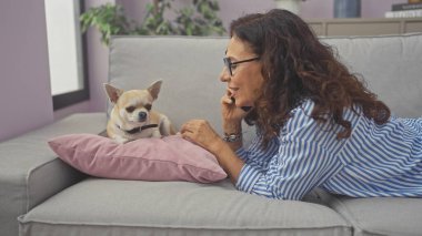 Orta yaşlı bir kadın, kapalı bir koltukta Chihuahua 'sının yanında telefonla konuşuyor..