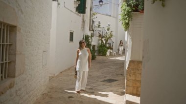 Genç bir İspanyol kadın locorotondo, puglia, italya 'nın büyüleyici eski sokaklarında geziniyor, güzel beyaz mimariyi ve güneş ışığındaki Avrupa atmosferini takdir ediyor..