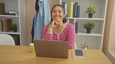 Ev ofis ortamında dizüstü bilgisayarlı gülümseyen İspanyol kadın, sıradan profesyonellik yayıyor..
