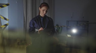 Kapalı bir suç mahallini araştıran odaklanmış bir kadın. Gece vakti uyarı bandıyla işaretlenmiş..