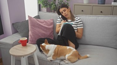 Genç bir İspanyol kadın, Chihuahua köpeği eşliğinde evinin oturma odasında notlar alırken telefonla konuşuyor..