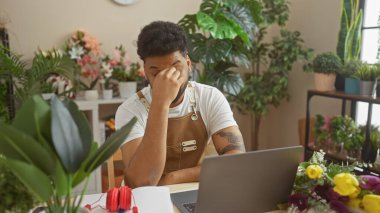 A stressed man with a tattoo is contemplating issues in a flower shop surrounded by plants and bouquets. clipart