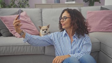 A middle-aged woman takes a selfie with her chihuahua in a cozy living room. clipart