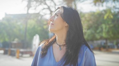 Olgun İspanyol kadın güneşli bir şehir parkının yeşilliğinin tadını çıkarıyor..