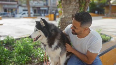 Yakışıklı İspanyol adam güneşli şehir parkında köpeğini okşuyor.