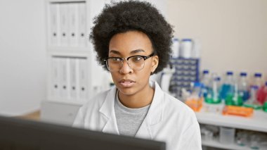 Etrafı ekipmanlarla çevrili bir laboratuvar ortamında çalışan odaklanmış Afrikalı Amerikalı kadın bilim adamı..