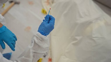 A forensic investigator collects evidence at a crime scene wearing protective gloves and a white suit. clipart