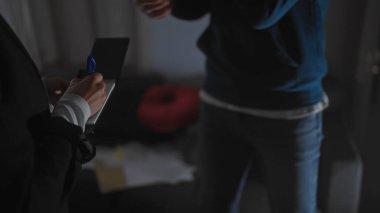 Bir kadın müfettiş, kapalı bir suç mahallinde loş aydınlatılmış bir adamın sorgusu sırasında notlar yazar..