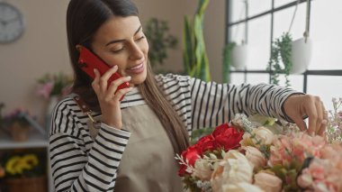Parlak bir oturma odasında çiçekleri düzenlerken telefonda konuşan İspanyol kadın.