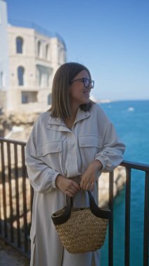 Genç İspanyol bir kadın polignano 'da güzel bir günün tadını çıkarıyor. Bir kısrak, puglia, İtalya manzaralı bir okyanus manzarası ve arka planda tarihi bir mimari.