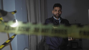 Ciddi bir İspanyol adam, oturma odasının karşısındaki kapalı bir suç mahallinde elinde bantla dikiliyor.