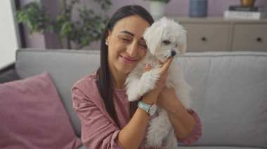 Gülümseyen genç bir kadın samimi bir oturma odasında tüylü beyaz bir bizon Malta sosu tutuyor..