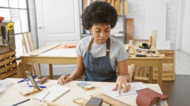 Afro-Amerikan kadın marangozluk stüdyosunda çeşitli ahşap işçiliği aletleri ve projeleriyle özenle çalışıyor..