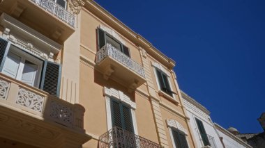 Zarif balkonlar ve panjurlar, eski Puglia, İtalya 'da açık mavi gökyüzüne karşı iki katlı büyüleyici bir binayı süsler..