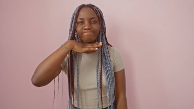 Örgülü, etkileyici siyah bir kadın izole edilmiş pembe bir arka plana karşı boğazını kesen bir jest yapıyor..