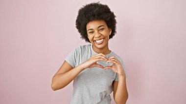 Kıvırcık saçlı Afrikalı Amerikalı kadın pembe arka planda elleri olan bir kalp yapıyor..