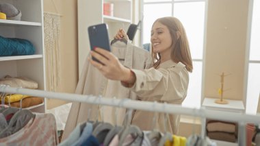Gülümseyen kadın, parlak, modern bir elbise odasında bluzuyla selfie çekiyor.