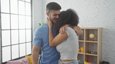 Erkek ve kadın, büyük pencereli ve şık dekorlu, modern bir oturma odasında sevgiyle kucaklaşıyorlar..