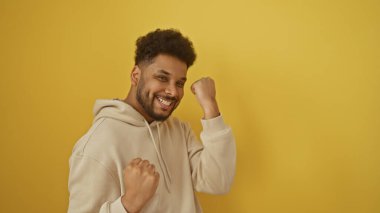 Neşeli bir siyah adam, parlak sarı bir arka plana karşı zafer kutluyor, pozitif bir hava ve güven yayıyor.